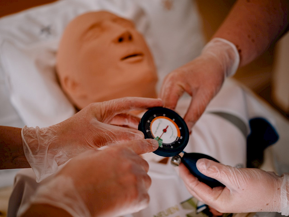 Pflegefachkräfte üben an einer Schulungspuppe den Cuffdruck zu messen