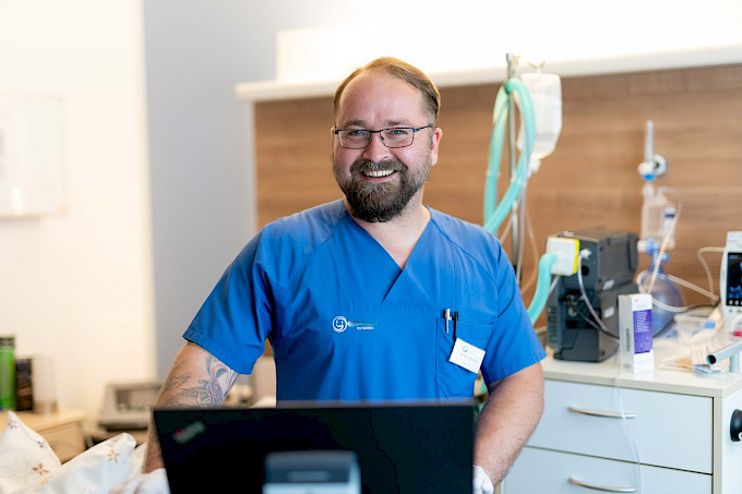 Lächelnde Pflegefachkraft steht im Patientenzimmer Im Hintergrund sind einige Geräte der Intensivtherapie zu sehen